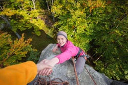 A male rockclimber is helping a young beautiful female climber to reach a peak of mountain. Man giving a hand to the woman.