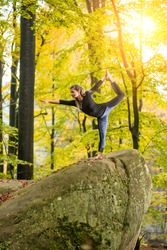 Yoga outdoors - sporty fit woman doing asana Narajasana in autumn park on the big boulder
