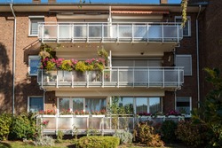 Traditional European residential house with balconys with colorful flowers and flowerpots. Facade of a residential building with well-kept loggias and balconies in sunny weather in Krefeld, Germany.