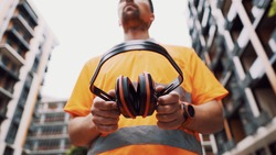 Construction worker with ear muff working at construction site. Worker puts on ear defenders to protect against sound. Taking care of health, safety at work. Earplugs. Too loud sound, hearing damage.