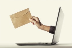The human hand with envelope stick out of a laptop screen. Concept of correspondence, feedback, advertising via internet.