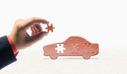 The hand inserts the last piece into the car-shaped puzzle. Car buying, repair, warranty service. Concept.