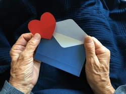 A blue envelope and a red heart in the hands of an elderly woman. Holiday greetings