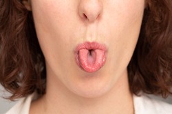 A closeup view of a young Caucasian lady sticking out her tongue and curling the sides up.