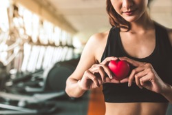 Happy sport woman holding red heart in fitness gym club. Medical cadio heart strength training lifestyle. Pretty female sport girl workout exercise. Cardiac healthy and wellbeing. Massage ball in hand
