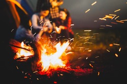 Sparking bonfire with tourist people sit around bright bonfire near camping tent in forest in summer night background. Group of student at outdoor fire fuel. Travel  activity and long vacation weekend