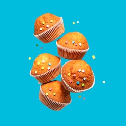 Levitating delicious vanilla cupcakes. Cupcakes in paper liners with colorful icing stars fly on blue background.