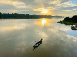 An early Morning view of a fisherman riding boat through Periyar River in Kerala India. The Sun rise adding beauty to the Nature.