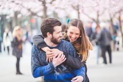 Young hipster couple embracing and smiling in Stockholm with cherry blossoms at Kungstradgarden, the swedish for Kings Garden. Love and friendship concepts with a hipster theme.
