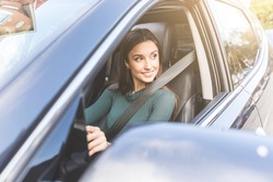 Young woman driving a car in the city. Portrait of a beautiful woman in a car, looking out of the window and smiling. Travel and vacations concepts