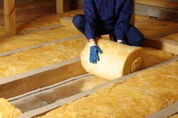 Construction worker thermally insulating house attic with glass wool 