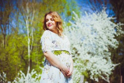 Beautiful pregnant woman walking in the flowers garden in the spring