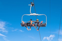 People riding ski chairlift. View from below. Group of people traveling on ski lift on top of mount for enjoing ski and snowboard. Winter sport, travel and vacation concept. 