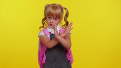Kid primary school girl say no hold palm folded crossed hands in stop gesture, warning of finish, prohibited access, declining communication, body language, danger on yellow background. Back to school