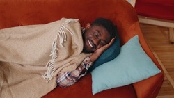 Candid casual african american young man sleeping quietly in bedroom at home. Happy adult guy smiling, lying on bed, sleeping on a comfortable sofa and pillow, resting peacefully. Healthy sleep alone