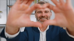 I love you. Mature business man makes symbol of love, showing heart sign to camera, express romantic feelings, express sincere positive feelings at home office workplace. Charity, gratitude, donation