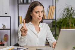 Caucasian young business woman working on laptop computer shakes finger, saying No be careful scolding and giving advice to avoid danger mistake disapproval sign at office. Confident freelancer girl
