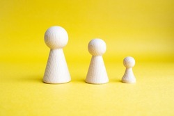 Three pawns different sizes lined up side by side on yellow background, concept idea for business or school life success or growing, wooden pawns represent business person or student, selective focus