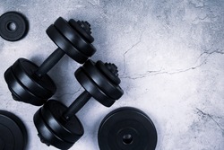Top view of black dumbbells and different weight plates on gray textured background. Flat lay. Fitness or bodybuilding sport training concept. Copy space.