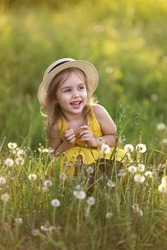 Cute fun little girl in a straw hat has fun on a summer field with dandelions . Child having activity fun outside. Concept of a healthy child without allergies. High quality photo