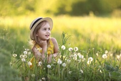 Cute little girl in a straw hat has sits on a summer field with dandelions. Child having activity fun outside. Concept of a healthy child without allergies. High quality photo. High quality photo