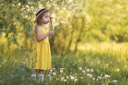 Cute little girl in a straw hat blowing on a dandelion flower on the nature in the summer. Child having activity fun outside. Concept of a healthy child without allergies. High quality photo