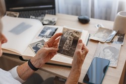 Senior woman is looking her own old photos at home. Elderly woman has got smile while remembering how young and beatiful she was. Selective focus. Photo was taken in 1953