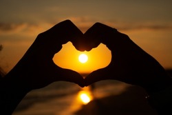 Heart sign with hands at the sunset on the beach next to the sea