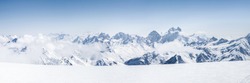Panoramic view of a Mt. Elbrus ski slope and snowy Greater Caucasus mountains on the horizon at winter cold sunny day.