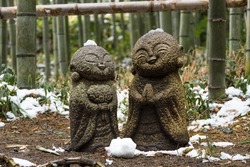 Two little small buddhist stone status in bamboo forest, Arashiyama, Kyoto, Japan. Kind, smiling face Jizou putting hands together. Winter snow. 