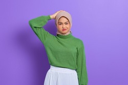 Beautiful young Asian woman in green sweater confused about a question, thinking with hand on head isolated over purple background