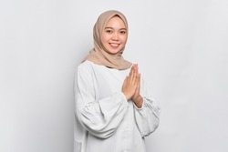 Smiling young Asian Muslim woman gesturing Eid Mubarak greeting isolated over white background