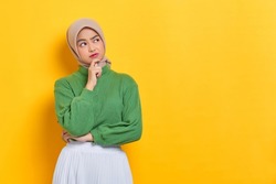 Pensive beautiful Asian woman in green sweater thinking about something and looking away isolated over white background