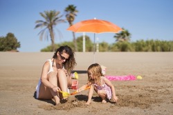 a woman and her young daughter playing with the sand to bury their feet on the beach