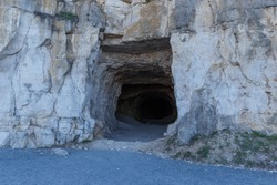 The concept of cave people's habitat. A stone wall with a dark hole, the entrance to the cave. Historical mineral mine.