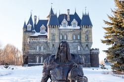 A Viking with an axe and helmet in his hands poses in winter against the background of a castle. A medieval-style concept, bronze Viking statue. Travel and tourism.
