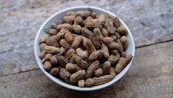 a bowl of roasted peanuts on a wooden background