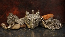 Silver amulet with the head of a wolf with a Viking ornament on the background of stones and amulets Thor's hammer symbol of fear selective focus mysticism abstraction