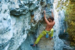 muscular man rock climber in bright yellow pants climbing the challenging route on the cliff in forest. strong bearded rock climber climbs on a rocky limestone wall, side view. sport and active