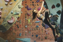 Young female climber Climbing Inside climbing Gym. slim pretty Woman Exercising At Indoor Climbing Gym Wall. Concept of strength, sport, healthy lifestyle.
