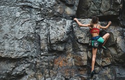 young slim muscular woman rockclimber climbing on tough sport route, searching, reaching and gripping hold. climber makes a hard move. outdoors rock climbing and active lifestyle concept
