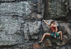 attractive slim muscular young woman rockclimber climbing on tough sport route on granite cliff, resting and chalking hands. outdoors rock climbing, exercising and active lifestyle concept. 