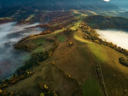 Aerial top view from above on amazing hills, mountain range in valley bottom at early morning with low clouds.