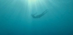 Woman silhouette floating underwater in beautiful blue sea with sun rays. Freediving diving on a breath hold. Unfocused image