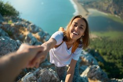 Outdoor portrait smiling girl hiker climbing up on cliff and holding helping hand for reaching to summit. Active lifestyle adventure concept