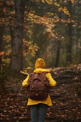 Female in dark forest wearing yellow rain coat with backpack and looking away from camera. Moody autumn scencery with a young girl walking alone in woods