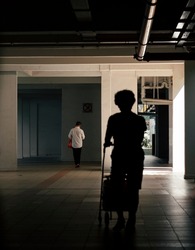 Pushing groceries cart at void deck of HDB flat in shadow and light