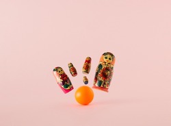Russian dolls known as matryoshka or babushka as the pins knocked by the orange bowling ball on a pink background. Minimal concept.
