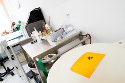 White biohazard medical container with yellow hazard symbol filled with medical waste in a medical room.