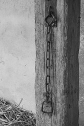 On a wooden beam hangs a rusty chain with iron ring
